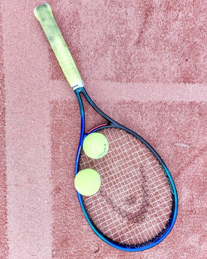 A racquet and two balls resting on a clay court